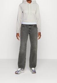 Svetle šedá zkrácená mikina s šňůrkami, kombinovaná s rovnými tmavě šedými džíny. Nosené s vzorovanými šedobílými teniskami.