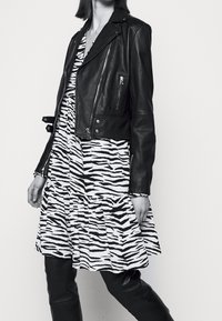 Giacca cropped in pelle nera sopra un vestito a strisce in bianco e nero con design a balze. Tessuto liscio; maniche aderenti.