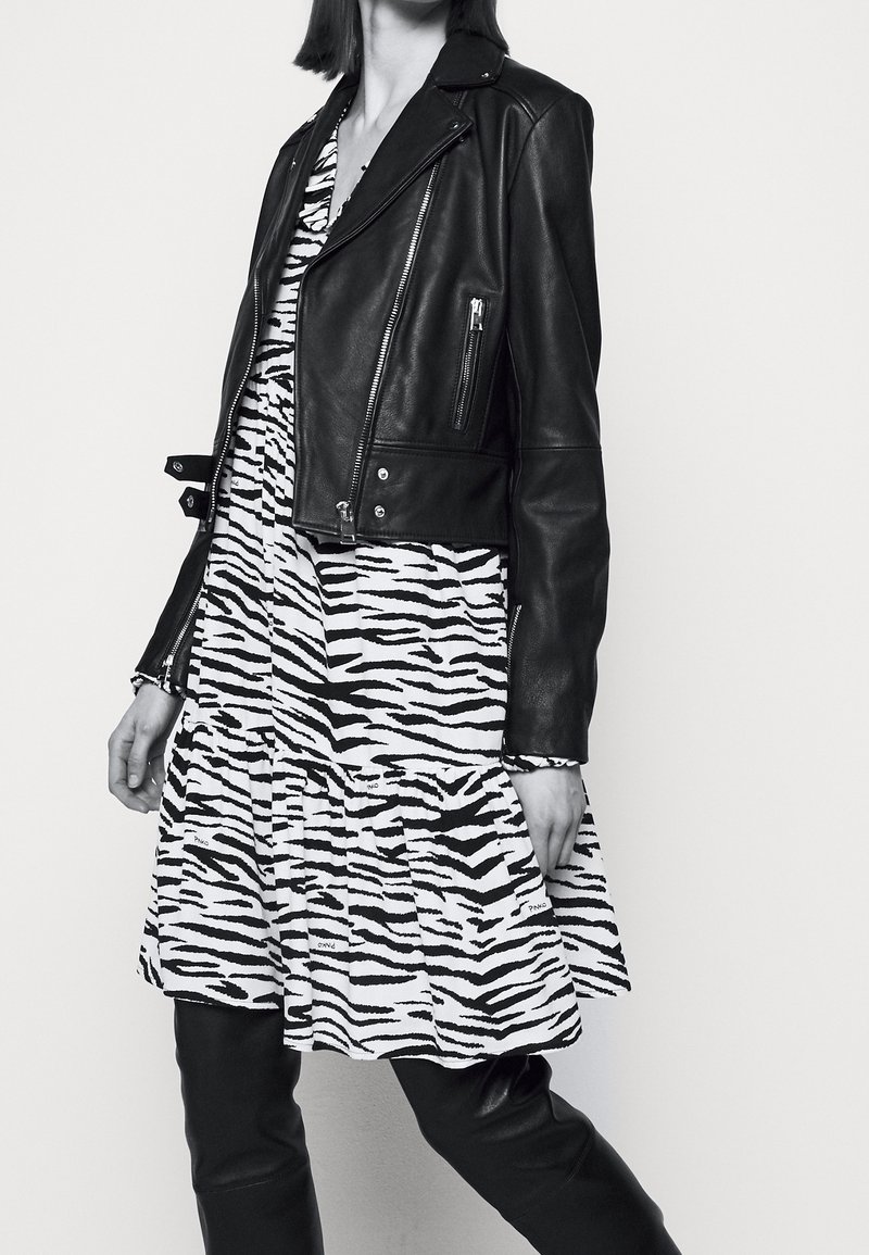 Giacca cropped in pelle nera sopra un vestito a strisce in bianco e nero con design a balze. Tessuto liscio; maniche aderenti.