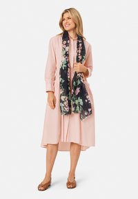 Peach cotton dress with a button-down front and gathered waist, paired with a black floral scarf featuring pink and green accents. Brown sandals.