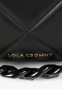 Black faux leather bag with quilted design, featuring a gold brand logo "LOLA CSDMNT" and a twisted black chain strap.