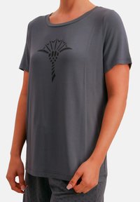 Szara koszulka z krótkim rękawem i okrągłym dekoltem, z czarnym graficznym wzorem stylizowanego drzewa na przodzie. Miękka tekstura tkaniny.