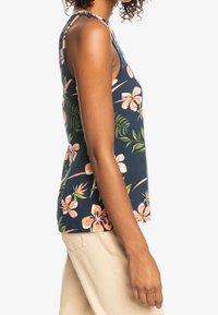 Ärmlös marinblå tanktop med stora rosa blommor och gröna bladtryck. Tillverkad av mjukt, lätt tyg med rund halsringning.