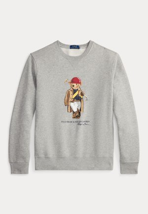 Šviesiai pilkas džemperis su spalvingu meškos piešiniu, dėvinčios kepurę ir darbo drabužius, su briaunuotomis rankogaliais ir apačia. Įtraukta užrašas „Polo Bear by Ralph Lauren“.