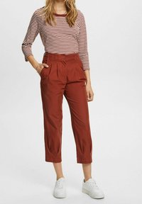 Rode cropped broeken met plooien, gecombineerd met een witte en kastanjebruine gestreepte lange mouwtop. Afgewerkt met witte sneakers.