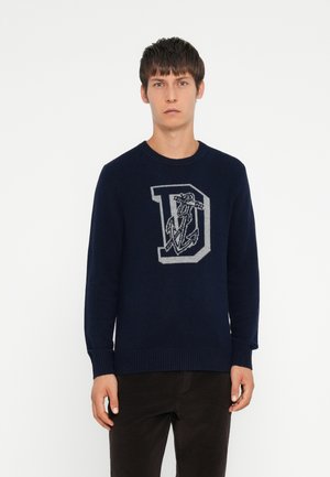 Marineblauwe trui met ronde hals, geribbelde manchetten en zoom. Heeft een grote grijze letter "D" met een ankerontwerp gebreid in het midden.