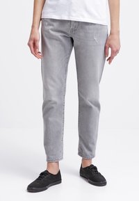 Grå denimjeans med rak benstil, med subtil slitning och en mjuk textur. Matchas med svarta sneakers.