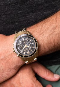 Kronograaf kellaga, millel on roostevabast terasest korpus ja kullatoonilised aksessuaarid. Must tekstuuriga kelladial, millel on hõbedased märgid ja kolm aladiagrammi. Hõbedane käevõru.