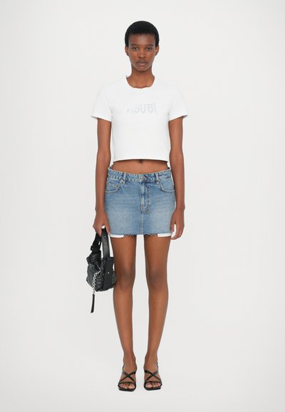 Tricou alb scurt cu logo, fustă mini din denim, sandale negre cu barete și o geantă mică alb-neagră cu model. Textură netedă, design casual.