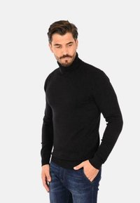 Maglione a collo alto nero in tessuto morbido con maniche lunghe e design aderente, abbinato a jeans blu. Stile semplice e classico.