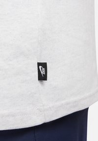 Witte katoenen t-shirt met een gestikte zoom en een zwart Nike-logo label op de onderlinkerkant. Zacht, textuur materiaal.