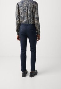 Marineblauwe slim-fit broek met een gladde textuur, met twee achterzakken. Gemaakt met een gestreepte overhemd met lange mouwen en zwarte schoenen.
