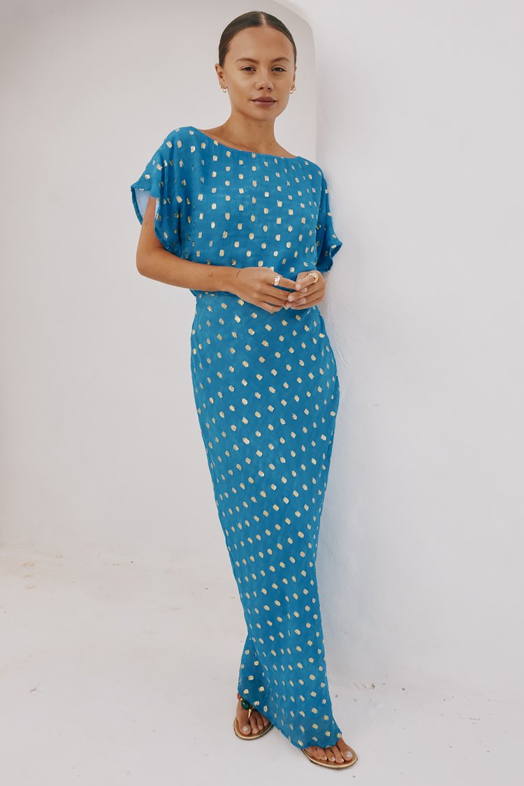 Rochie lungă albastră, cu mâneci scurte și croială lejeră, având un model cu puncte aurii. Material neted și ușor, cu o siluetă dreaptă.