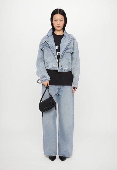 Svijetloplavi traper jakna s krojenim dizajnom, dva prednja džepa, nosi se preko crne majice s grafikom. Opuštene svijetloplave traperice i crna torba.