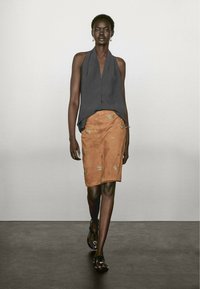 Ärmelloses graues Oberteil, A-Linien-Design, kombiniert mit einem beige-suede Rock, der goldene gestickte Blattmuster und schwarze Sandalen aufweist.