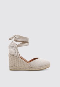 Zapato de cuña de esparto beige con parte superior de tela texturizada, mediopié de yute trenzado y cintas en el tobillo para un ajuste seguro.