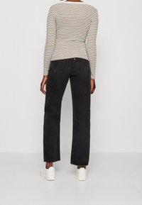 Schwarze gerade Jeans mit hoher Taille, kombiniert mit einem langärmeligen Oberteil mit bunten Streifen. Weiße Sneakers runden das Outfit ab.