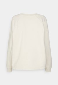 Krémová mikina s kulatým výstřihem, žebrovanými manžetami a volným střihem. Má hladkou texturu a raglánové rukávy.