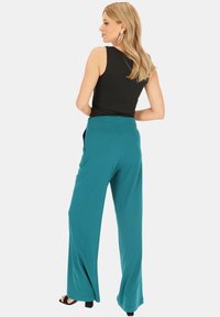 Turkusowe spodnie o szerokich nogawkach z gładką teksturą i wysokim stanem. W zestawieniu z czarnym topem bez rękawów i czarnymi sandałami na obcasie.