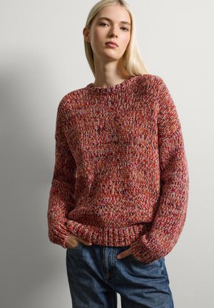 Suéter de punto grueso en tonos de rojo, naranja y rosa. Cuello redondo, puños anchos y un corte relajado. Combinado con jeans de mezclilla.