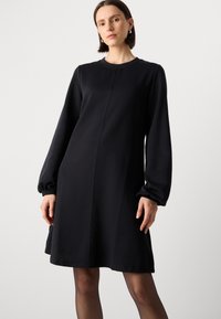 Zwarte langenaamijke jurk met een ronde halslijn, relaxte pasvorm en een lichte A-lijn silhouet; gladde textuur en subtiele naaddetails.