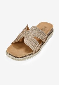 Tan slide sandal with a textured glitter band featuring wavy cutouts. Espadrille-style jute sole adds natural detail.