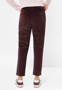 Burgundské kordové kalhoty s rovný střih, s zadními kapsami a mírně zúženým lemem, v kombinaci s bílými a burgundskými teniskami.