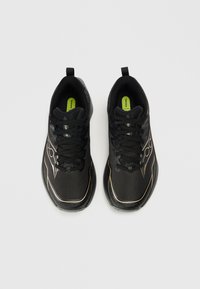 Zwarte sportschoenen met een bovenwerk van mesh, voorzien van zwarte veters, groene inlegzolen en metalen goudkleurige accenten langs de zool en zijkanten.