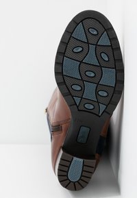 Bota de cuero marrón con suela de caucho texturizada que presenta detalles en azul y un patrón en zigzag, equipada con una cremallera lateral para un acceso fácil.