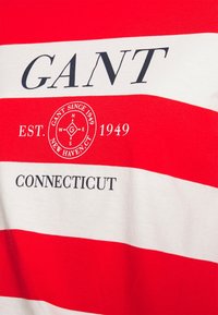 Punavalkoraidallinen T-paita, jossa pyöreä pääntie, "GANT"-logo, pyöreä merkki ja "CONNECTICUT"-teksti painettuna tummansinisellä.