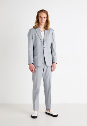 Light gray suit with a single-button blazer and matching trousers. Worn over a white top. Pairs with white shoes featuring black soles.