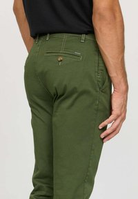 Chinos vert olive à coupe slim, dotés d'une poche arrière avec fermeture à bouton et de coutures contrastées le long des coutures.