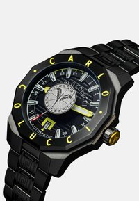 Schwarze automatische Armbanduhr mit achteckigem Zifferblatt, gelben Akzenten, strukturiertem Ziffernblatt, silbernem Logo in der Mitte und gemustertem schwarzem Metallarmband.