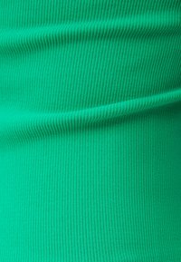 Tessuto a coste di colore verde brillante, caratterizzato da una consistenza morbida e linee verticali, con curve e pieghe fluide.