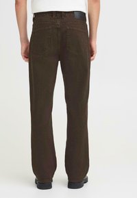 Brune denimbukser med rett ben-design, synlig søm og to baklommer. Har en midjebåndlabel, subtil tekstur og en ren finish.