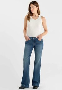 Jean évasé de couleur bleu moyen avec une texture lisse, associé à un débardeur blanc ajusté. La tenue présente un design classique.