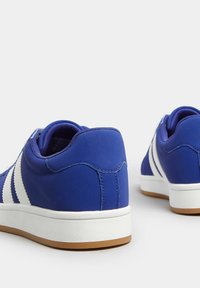 Niebieskie buty sportowe z białymi paskami, wykonane z gładkiego materiału syntetycznego, z gumową podeszwą oraz teksturowanym tyłem dla lepszej przyczepności.