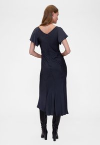 Szatén sötétkék tengerészkék ruha rövid lepel ujjakkal, V-alakú hátrésszel és bővülő szegéllyel, varrás nélküli kialakítással és rejtett cipzáras záródással.