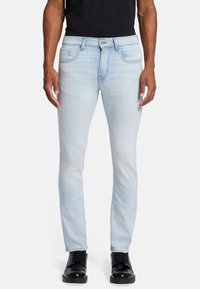 Jasnoniebieskie jeansy o slim fit, z przednimi kieszeniami, zapinane na guziki oraz delikatnym akcentem wyblaknięcia. W połączeniu z czarnymi sznurowanymi butami.