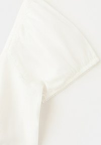 Mânecă scurtă de cămașă din bumbac alb, cu cusături vizibile la șină, pe un fundal deschis.