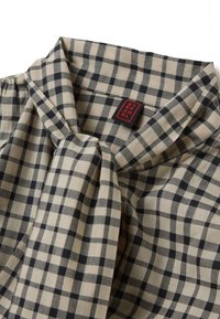 Beige and dark blue checkered blouse with a tie collar. Made of fabric with a smooth texture. Features a red brand label.