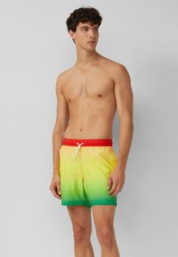Zwemshorts in een gradient van geel naar groen met een rode elastische tailleband en witte trekkoord, gemaakt van een gladde, lichte stof.