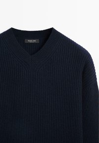 Maglione a maglia blu navy con scollo a V e texture a coste. Presenta un'etichetta del marchio all'collo. Realizzato in un materiale morbido.