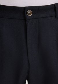 Granatowe spodnie z teksturowanej tkaniny, z metalowym zapięciem i schludnym pasem. Brak widocznych kieszeni i wzorów.