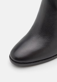 Černá kožená bota s špičatou špičkou a texturovaným povrchem. Nabízí hladký povrch a jemný šev podél podešve.