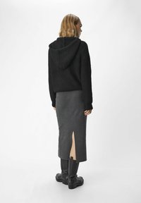Zwarte geribbelde hoodie-sweater gecombineerd met een grijze rok met een zijsplit. Model draagt zwarte chunky laarzen en is van achteren weergegeven.