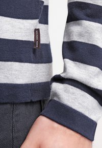 Marinblå och grårandig tröja i stickad kvalitet med rund halsringning, ribbade ärmslut och en liten logotyp på sidan.