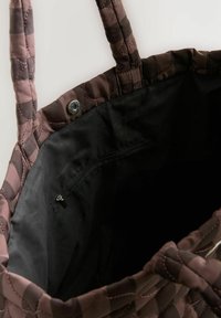 Gestepptes Tragetasche in verschiedenen Brauntönen mit rosa Steppnähten. Verfügt über ein schwarzes Innenfutter und eine Reißverschlusstasche. Zwei dicke Griffe.
