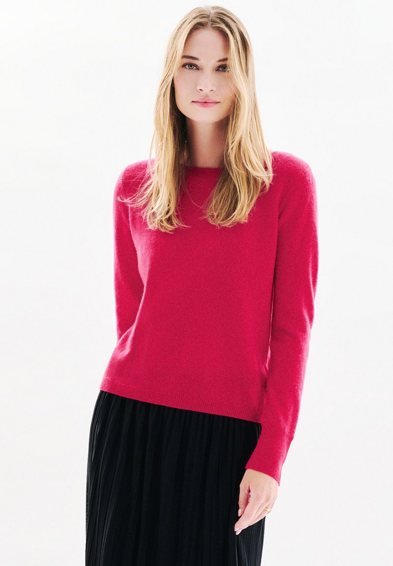 Maglione fucsia in morbido tessuto a maglia, con scollatura a girocollo e maniche lunghe. Abbinato a una gonna nera plissettata per creare un contrasto.