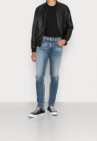 Svart läderbomberjacka, åtsittande svart skjorta, ljusblå slitage skinny jeans och svarta höga sneakers med vit sula.